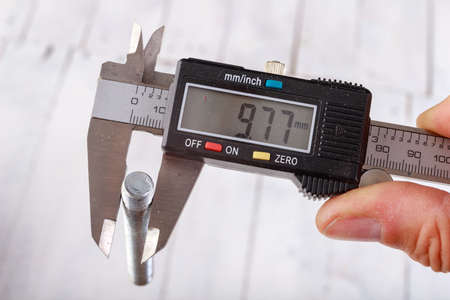 Measuring the thread diameter with an electronic caliper. Measuring accessories in a home workshop. Light background.の写真素材