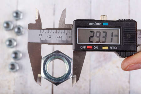 Measuring the nut width with an electronic caliper. Measuring accessories in a home workshop. Light background.の写真素材