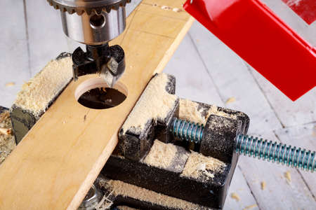 Drilling in wood with a cup drill. Minor carpentry work in a home workshop. Dark background.の写真素材