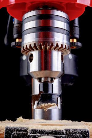 Drilling in wood with a cup drill. Minor carpentry work in a home workshop. Dark background.の写真素材