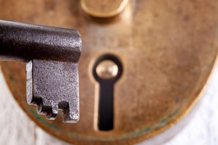 Old brass padlock and metal dark key. Old anti-theft security methods. Light background.の写真素材