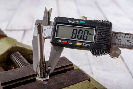 Threading a metal nut and measuring with an electronic caliper. Minor locksmith work in the workshop. Light background.の写真素材