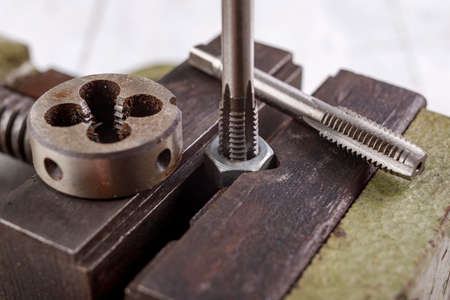 Threading a metal nut in a vice. Minor locksmith work in the workshop. Light background.の写真素材
