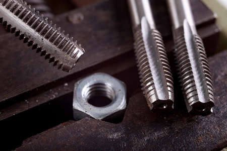 Threading a metal nut in a vice. Minor locksmith work in the workshop. Light background.の写真素材