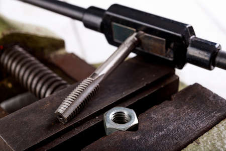 Threading a metal nut in a vice. Minor locksmith work in the workshop. Light background.の写真素材