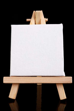Small easel with white blank cloth on a wooden table. Miniature painting accessories. Dark background.の写真素材