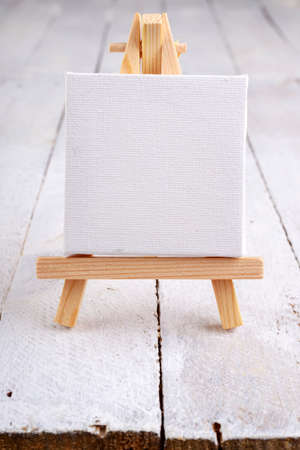 Small easel with white blank cloth on a wooden table. Miniature painting accessories. Light background.の写真素材