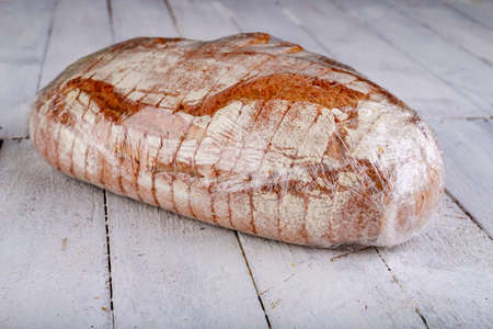 Well done bread wrapped in plastic wrap. Food prepared for transport. Light background.の写真素材