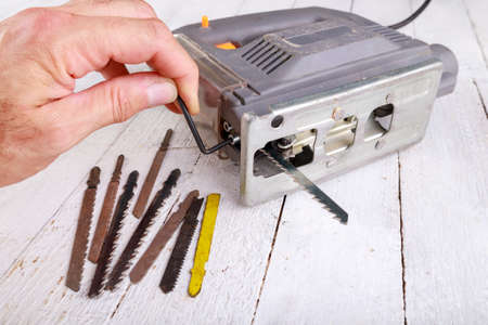Replacing the knife on a jigsaw for cutting wood. Carpentry accessories in a home workshop. Light background.の写真素材
