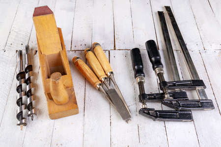 Wood planer, chisels and drill bits on a wooden table. Carpentry accessories in a home workshop. Light background.の写真素材