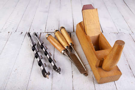 Wood planer, chisels and drill bits on a wooden table. Carpentry accessories in a home workshop. Light background.の写真素材