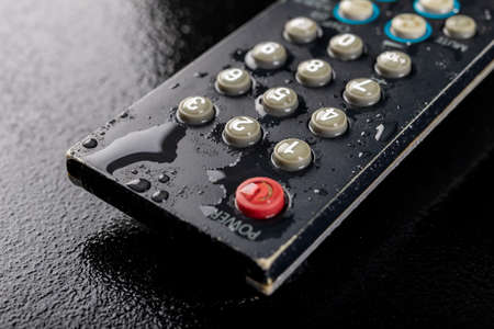 TV remote control with water drops. Water-poured electronic device. Dark background.の写真素材