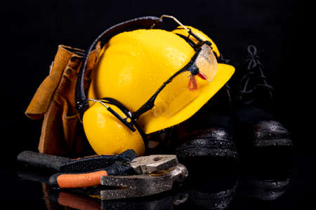 Wet work clothes and tools for the production worker. Raindrops on the helmet and glasses. Dark background.の写真素材