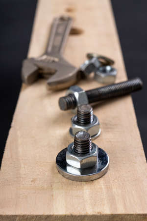 Metal bolts and nuts for joining wood. Tightening the screws with an adjustable wrench. Dark background.の写真素材