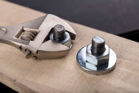 Metal bolts and nuts for joining wood. Tightening the screws with an adjustable wrench. Dark background.の写真素材