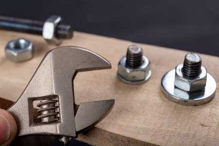 Metal bolts and nuts for joining wood. Tightening the screws with an adjustable wrench. Dark background.の写真素材