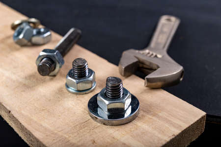 Metal bolts and nuts for joining wood. Tightening the screws with an adjustable wrench. Dark background.の写真素材