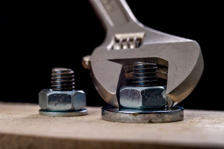 Metal bolts and nuts for joining wood. Tightening the screws with an adjustable wrench. Dark background.の写真素材