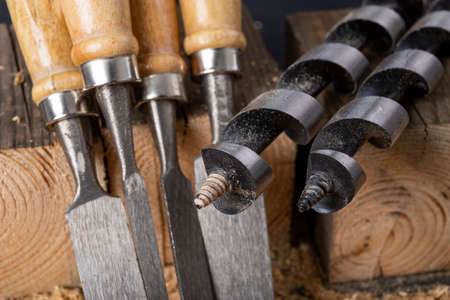 Chisels and wood drills laid on sawdust. Carpentry accessories in the workshop. Dark background.の写真素材