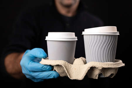 A set of hot drinks held by a courier. Delivery of goods ordered with home delivery. Dark background.の写真素材