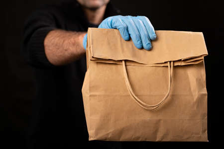 Paper bag held by a courier. Delivery of goods ordered with home delivery. Black background.の写真素材