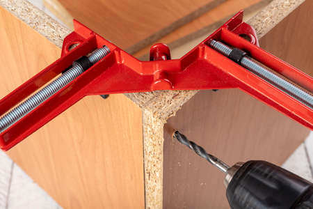 Chipboard in an angular carpentry clamp. Drilling in a furniture board. Light background.の写真素材