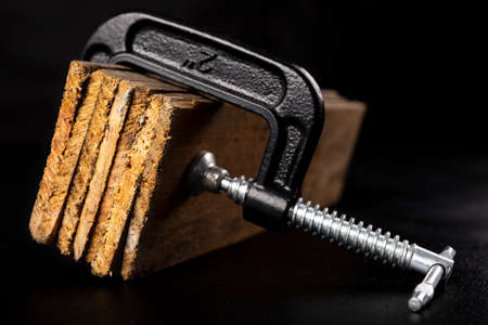 Small black joinery clamp for gluing wood. Carpentry accessories for work in the workshop. Dark background.の写真素材