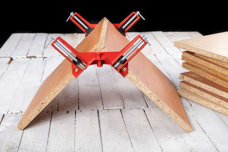 Chipboard in an angular carpentry clamp. Fixing the material for machining. Light background.の写真素材