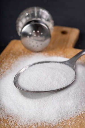 Metal spoon and spilled salt. A flavor enhancer added to dishes in home cooking. Dark background.の写真素材