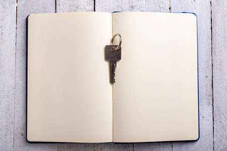 The key to the door in a single-family house placed on a paper notebook. Metal key for patent lock. Light background.の写真素材