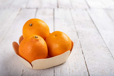 Tasty ripe tangerines in a wooden container. Exotic fruits on a wooden table. Light background.の写真素材