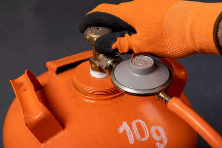 Unscrewing the propane-butane gas cylinder. Combustible gas used in households. Dark background.の写真素材