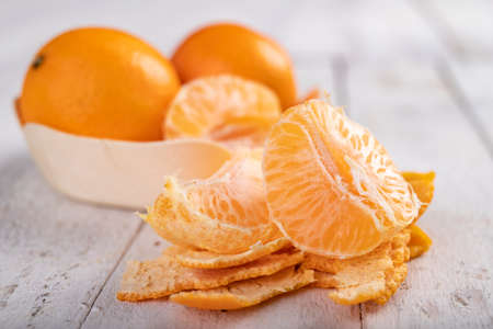 Tasty peeled mandarins in a wooden container. Exotic fruits on a wooden table. Light background.の写真素材
