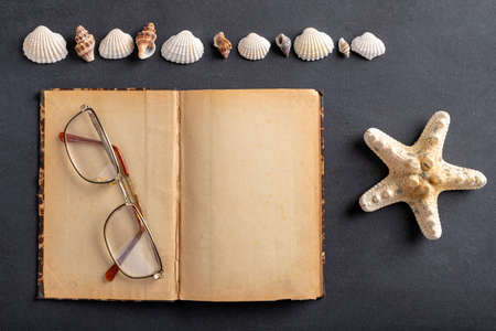 Old yellowed notebook, glasses and seashells. A place to save your holiday memories. Dark background.の写真素材