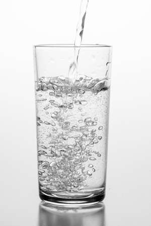 Pouring sparkling water into a glass. A container for storing liquids. Light background.の写真素材