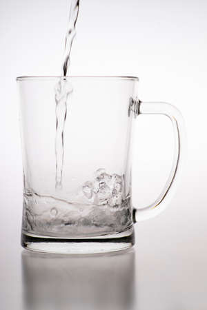 Pouring water into a mug. Glass container for weak carbonated alcohol. Light background.の写真素材