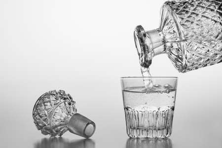 Pouring sparkling water from a carafe into a small glass. Decorative containers for serving water and alcohol. Light background.の写真素材
