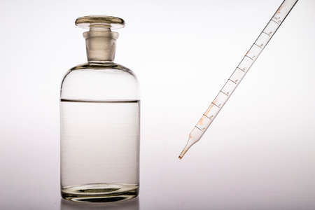 Glass pipette and chemical bottle. Accessories in the chemical laboratory. Light background.