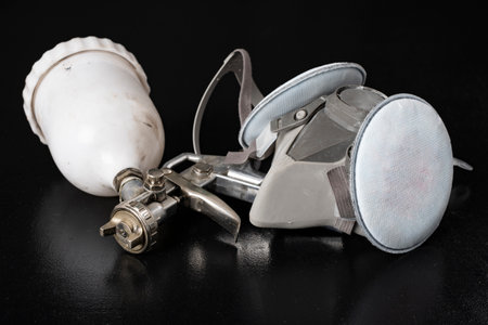 Metal spray gun for painting in a paint shop. Accessories for painting works and protective clothing. Dark background.の写真素材