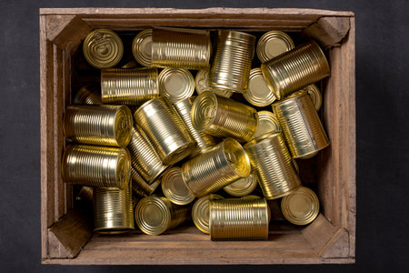 Metal cans of food in a wooden crate. Food stockpiled for hard times. Dark background.の写真素材