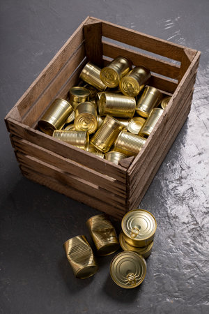 Metal cans of food in a wooden crate. Food stockpiled for hard times. Dark background.の写真素材