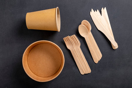 Wooden cutlery and paper disposable tableware on the table. Utensils used in the fast food bar. Dark background.の写真素材