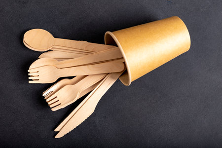 Wooden cutlery and paper disposable tableware on the table. Utensils used in the fast food bar. Dark background.の写真素材