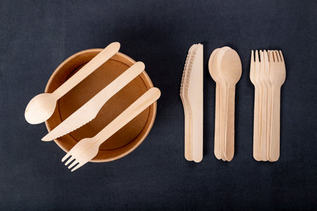 Wooden cutlery and paper disposable tableware on the table. Utensils used in the fast food bar. Dark background.の写真素材