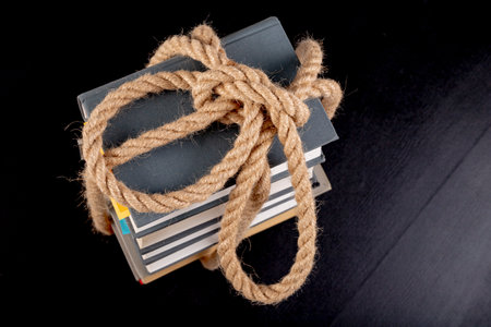 Thick books tied with a strong rope. A thick line around the paper. Dark background.