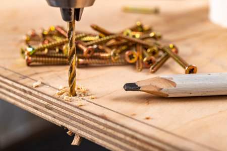 Drilling holes in plywood with a screwdriver. Minor carpentry work in the workshop. Light background.の写真素材