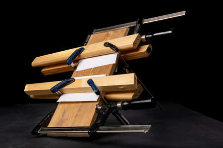 Gluing pieces of wood with carpentry glue. Boards in carpentry clamps. Dark background.の写真素材