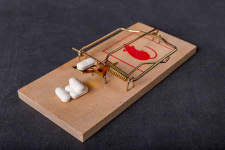 Medical tablets placed in a mousetrap. A trap for people in the form of pharmaceuticals. Dark background.の写真素材