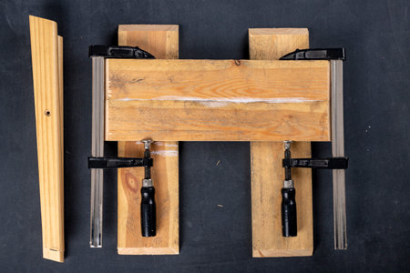 Gluing pieces of wood with carpentry glue. Boards in carpentry clamps. Dark background.の写真素材