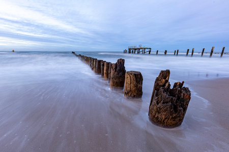 Foaming sea water pouring out onto the sandy shore. Sea wave crashing against a wooden breakwater. Autumn season.の写真素材